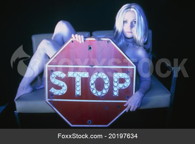 Naked young woman lying on couch, holding stop sign 