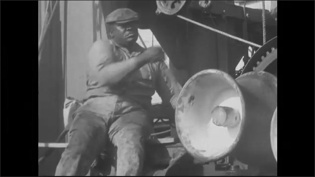 1930s: Man sitting by machinery, gears turning, man pulls lever. 