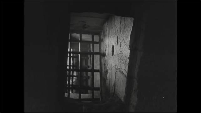 1940s: Dungeon door closes. Stone cell with barred window. Cross carving in cell wall.