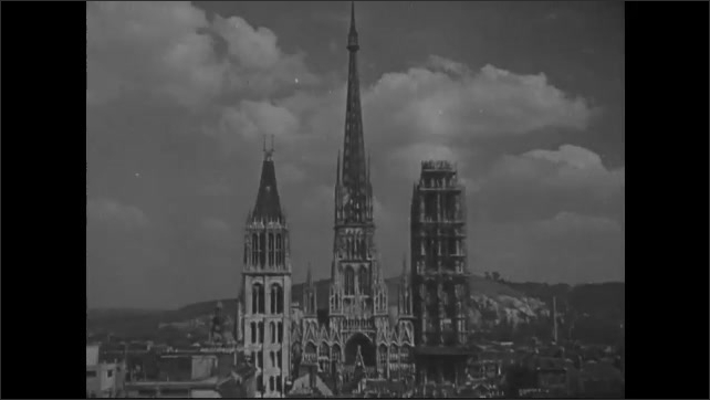 1940s: Cathedral spires loom over medieval buildings in city of Rouen. Ornate cathedral stands in center of city.