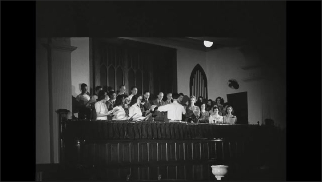 1940s: Teens dance on hall floor to music from jukebox. Choir rises in choir loft and sings. Conducting of choir.