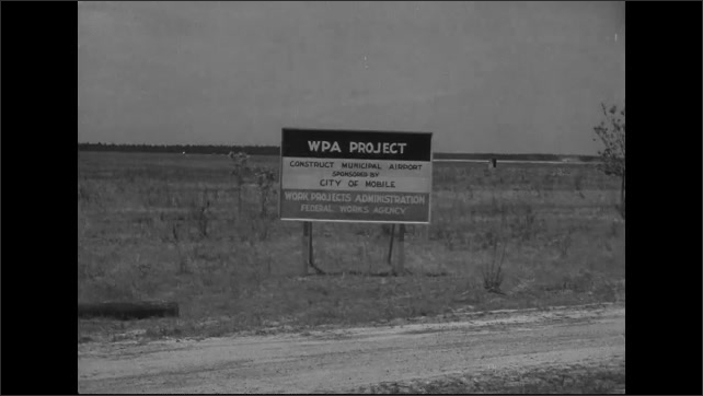 1940s: Dump trucks drive past a sign for airport construction. Sign for Gunter Field.