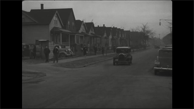 1930s: People walk past homes and parking lot along busy neighborhood sidewalk.