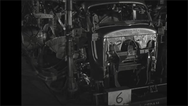 1930s: Using a suspended welding tool, worker makes a series of welds between the frame and body of a sedan.