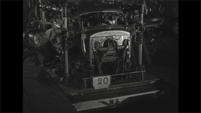1930s: Two workers, using suspended welding tools, wait as a sedan body comes into position.  As it does, the workers make a series of welds between the frame and body.