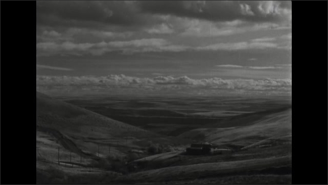 1940s: vista overlooking a vast distance of hills with clouds above, car driving over road looking over hills