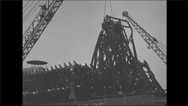 1940s: Crane lifts group of car chassis from back of train car. Crane ...