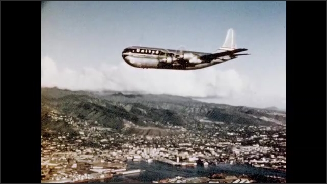1950s: United Airlines DC-6 Stratocaster flies over Diamond Head, Waikiki Beach and Honolulu city. Airplane lands on runway. 