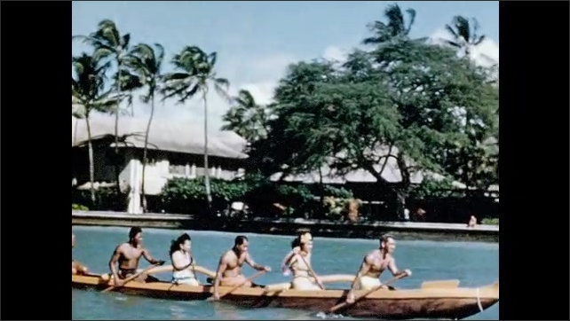 1950s: Outrigger canoe paddles past Royal Hawaiian Hotel, palm trees and back to Waikiki Beach club. 