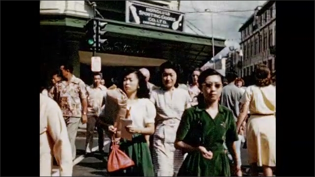 1950s: Pedestrians cross busy Honolulu street. Schoolchildren in schoolyard crowd towards camera.