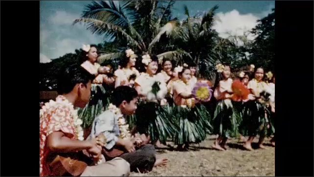 1950s: Schoolchildren in schoolyard crowd towards camera. Girls and women dance Hula. Group of women play ukelele and sing on lawn.