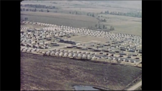 1950s: Bold narrative voice celebrates the transient life of mobile home dwellers over aerial views of housing development and chrome mobile home approaching large church barn.