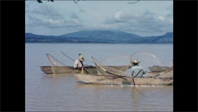 1950s: Small fishing boats skim along water in large lake by mountains; fishermen with large nets float in boats.