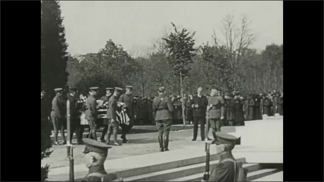 1910s Military officers carry casket past onlookers at ceremony. Men inter Unknown Soldier in monumental grave. Native American chief prays over grave. Military offers salute at graveside.