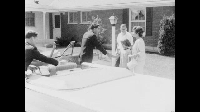 1960s: Three people in convertible pull into driveway of house. People greet people in car. Washing machine inside house.