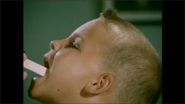 1950s: Little boy sits on doctors examination table. Medium shot of Doctor puts a tongue depressor in the boys mouth and examines his throat. Close-up of boy being examined. Doctor uses stethoscope.