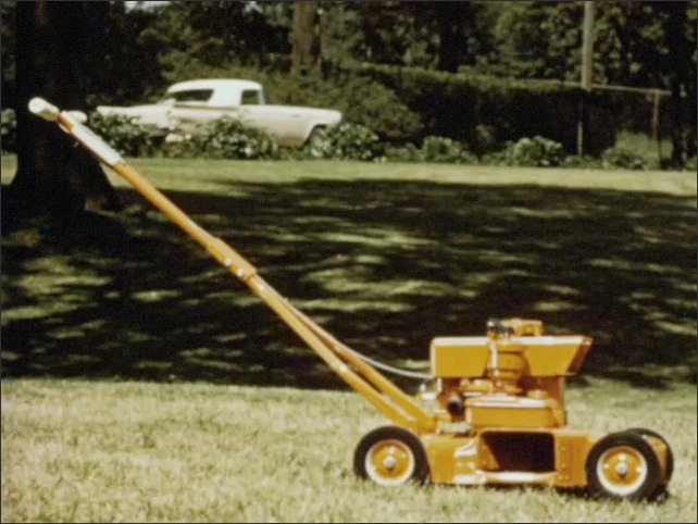 1960s:  A man stands in front of peg board display of rotary lawnmower parts. A shiny new lawnmower on lawn as classic car drives by. Man holds handles of mower, moves a switch back and forth.