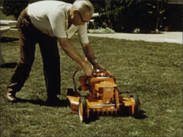 1960s: A yellow lawnmower on grass. The handlebar. An elderly man pulls the cord and starts the motor. He flips a switch on the handlebar. Man walks behind mower on autopilot.