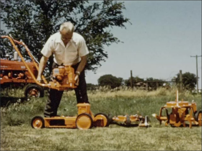 1960s: Man pushes lawnmower, stops, raises the clutch lever and a switch, stoops and flips a switch on the chassis. Man puts top of lawnmower on base as tractor drives by. Mower parts in grass.
