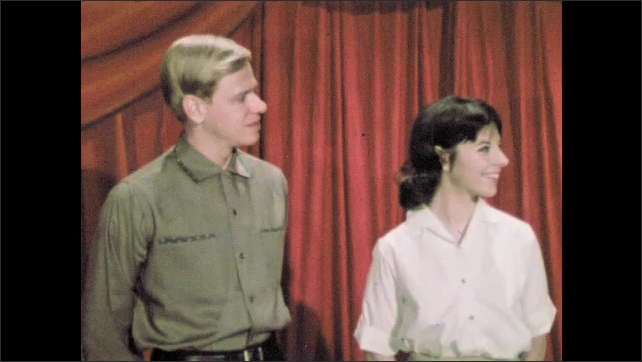1960s: Man smiling on stage. Man and woman on stage smiling. All three people walk off stage together.