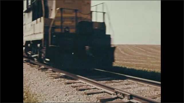 1970s: Grain travels down chute into tank. Man scoops grain from bottom of tank. Harvesters travel across field. Freight train. People work in factory.