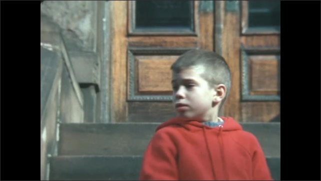  1960s: Italianate building, arched windows, elaborate decorative carving. Boy stands on stoop, bounces ball, turns, looks, leans on railing, smiles, walks down steps.