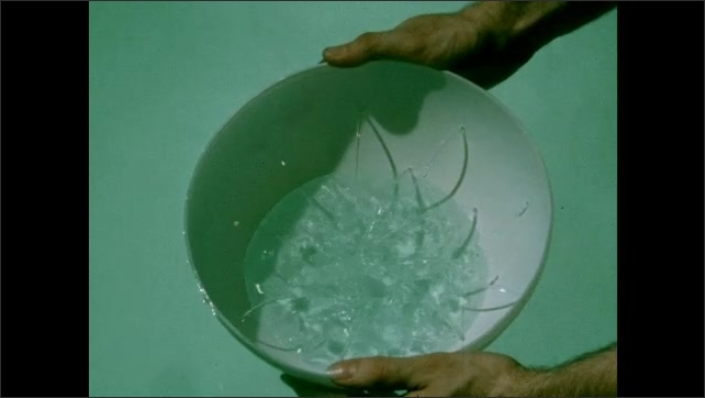 1950s: Hand holds chalk slate. Hands push bowl with holes into water. Water fills bowl through holes in surface. 