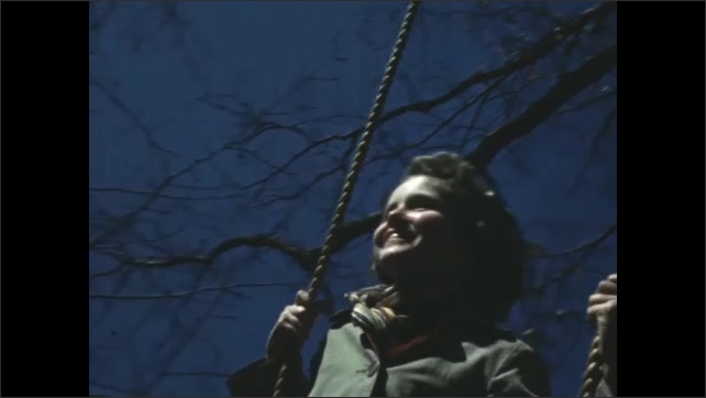 1950s: Boy pushes girl on swing with rope handles. POV swing movement in grass and trees. 