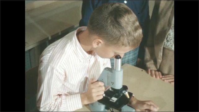 1950s: Students stand around kid looking into microscope. Kid looking into microscope. Trees in orchard. Man picks fruit from tree.