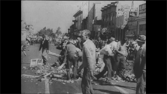 1920s: Men dump milk from bottles and crates onto side of road. Men smash crates in street. People march in protest down road.