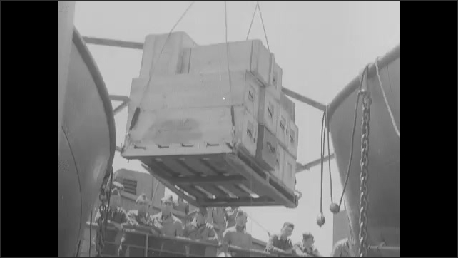 1940s: Boxes and cranes on deck of ship. Crane lifts boxes from ship to dock.
