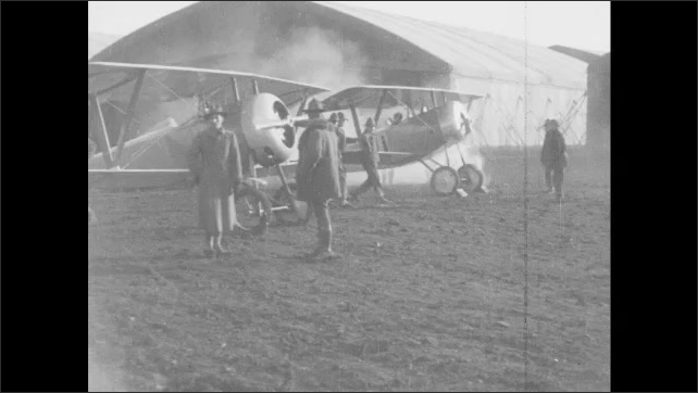 1910s France: Mechanic spins propeller.  Men work on airplanes.