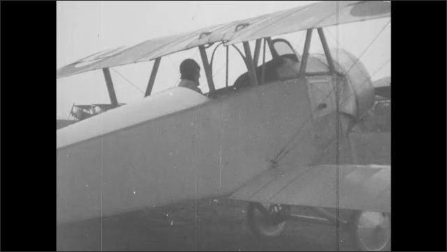 1910s France: Man climbs out of airplane and talks to pilot.  People watch man climb into plane.