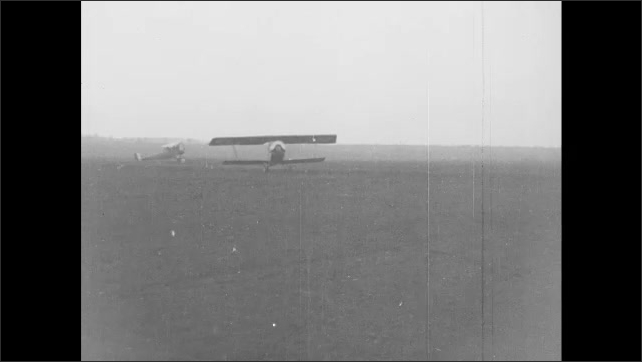 1910s France: Airplane takes off from field.  Men stand near plane.