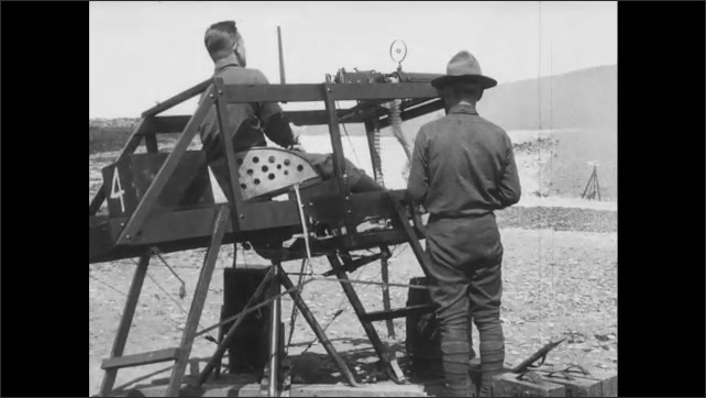 1910s France: Man practices controlling machine gun at firing range.  Officer feeds bullets into gun.  Men watch.
