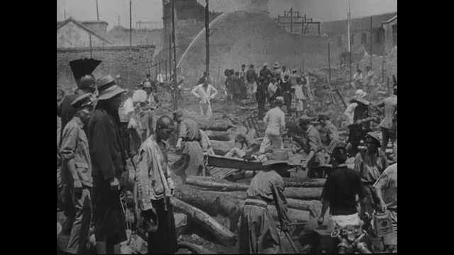 1940s China: People sift through rubble and debris, carry bodies away on stretchers. Man carries baby. People walk streets strewn with bodies. People load bodies onto truck. 