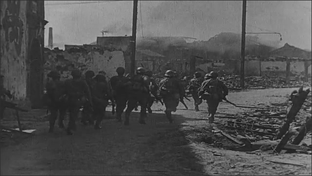 1940s China: Soldiers run through village, cannons fire. Explosion in field. Soldiers run through city, cannon fires. Village burns. Soldiers cheer. Soldiers and tank travel through wreckage of city. 