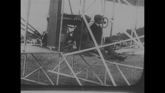 1900s: Wright Brothers sit in pilot's seat on airplane. Intertitle card. People prepare Wright Brothers airplane for flight.