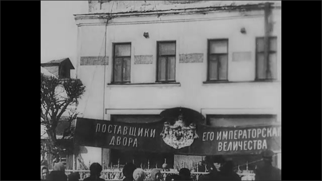 1910s: Intertitle. Sign is lowered from hanging on building. Crowd of people walking in street.