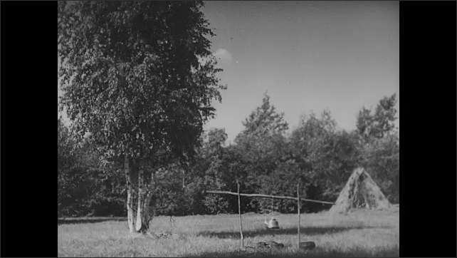 1910s: Row boats along shore. Grass hut. Grass hut. Kettle hangs above open pit fire. Shack building.