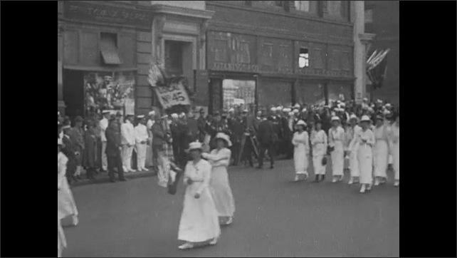1910s: Float in parade. Women in white walk in parade.