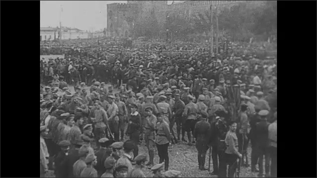 1910s Russia: Soldiers marching on field. Lenin shakes hands of men. Huge gathering of people in city square. Lenin addresses the people. Soldier holding flag. 