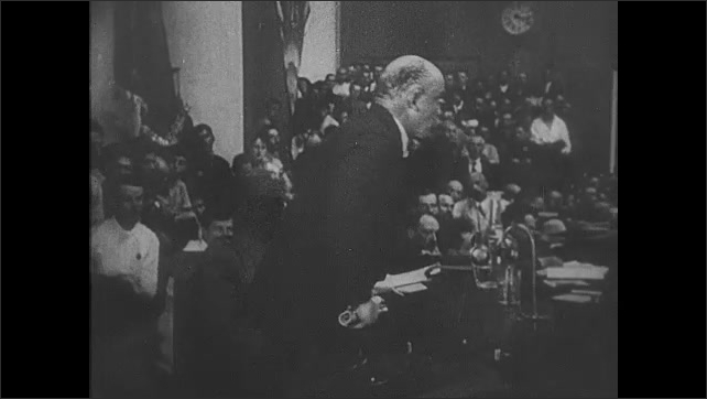 1910s Russia: Lenin speaks passionately from a dais in crowded room. Huge crowd stands and claps. 