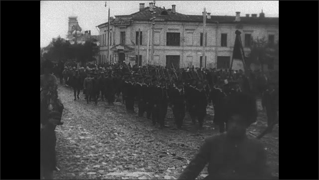 1910s USSR: Soldiers on horseback ride on railway platform. Soldiers march in uniform in the streets carrying banners and flags. Lenin in a fur hat in a crowd. Shipping cranes. 