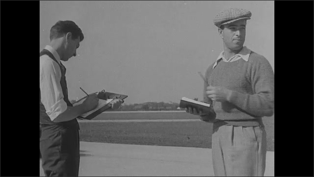1930s: Cars drive on test track. Men watch cars drive, write on notebooks. Cars drive on track.