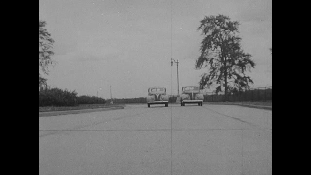 1930s: Cars drive on test track. Man watches, writes on paper. Cars on test track. Two cars come to stoop. Intertitle.