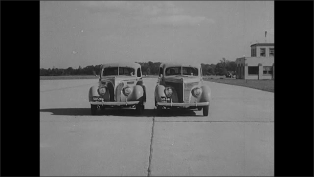 1930s: Two cars drive side by side on test track.