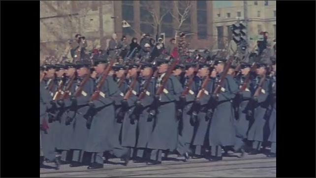 1960s Washington DC: Inauguration Day Parade. Men march in Revolutionary War uniforms, blow horns, play drums. Men march in gray Civil War uniforms, carry rifles. US Capitol Building.