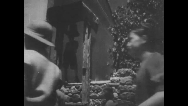 1950s Greece: Woman brings bouquet from bedroom to kitchen.  Women sit.  Boy rings bell.  Students walk into school building.  Men talk.  Arch.