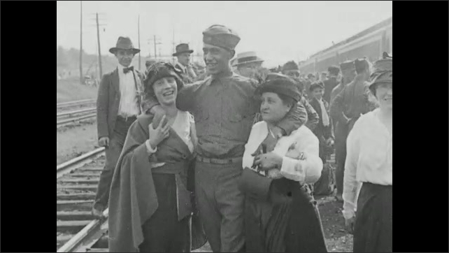1910s: People gather around train. Man in uniform stands in front of train, smiles. Soldiers pose with women. Solder kisses women. Soldiers wave. 